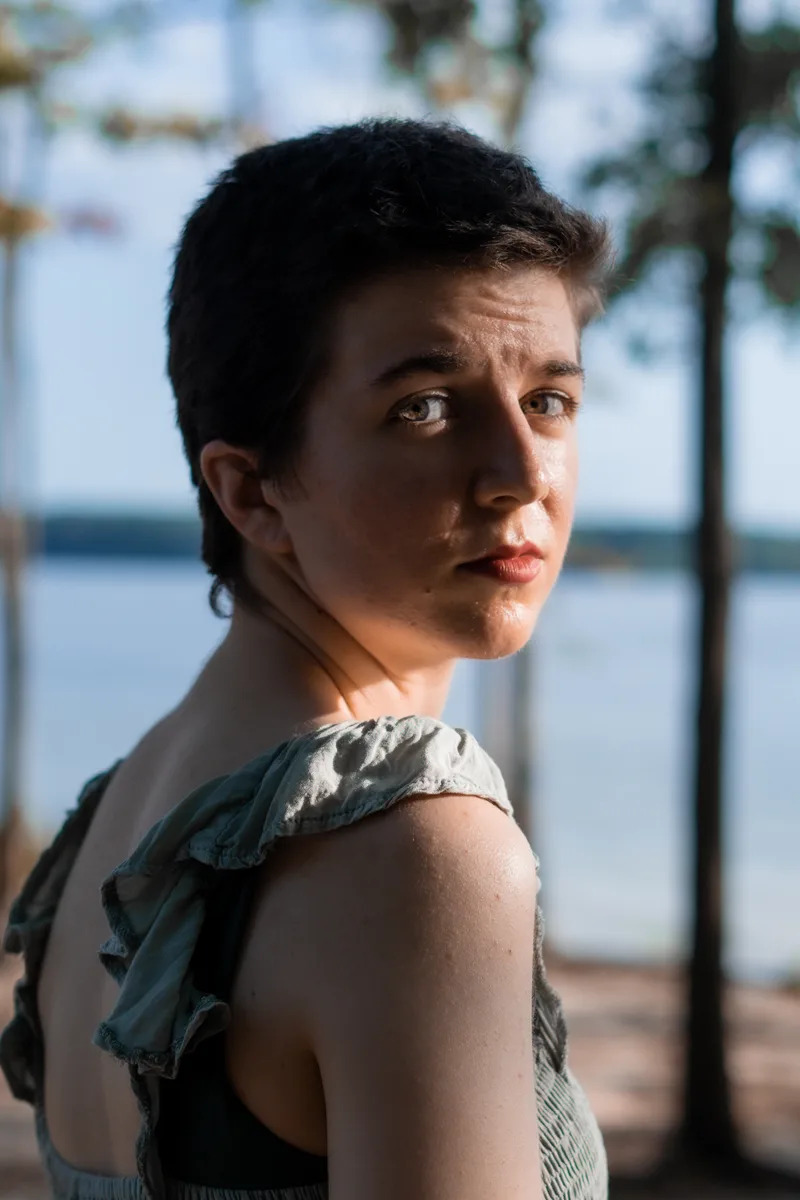 Headshot of white person with short dark hair, looking over shoulder at the camera. 
